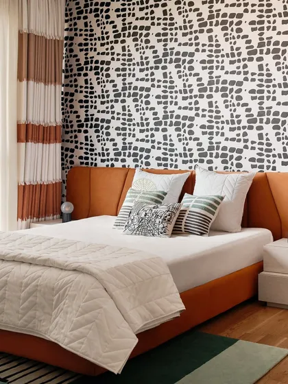 This bedroom makes a bold statement with a graphic black-and-white patterned wall behind an orange upholstered bed. The striped curtains add another layer of pattern, creating a vibrant and energetic space.