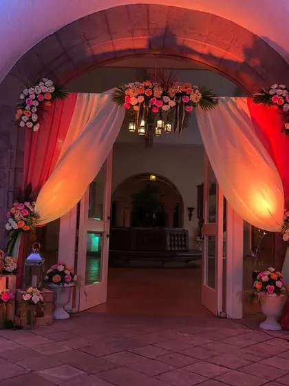 The entrance to this event features a beautiful combination of red and white draped fabric over the doorway. The look is enhanced with floral arrangements and warm uplighting for a welcoming feel.