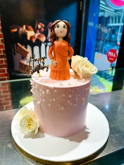 The full cake featuring the custom figurine, decorated with fresh white roses and edible pearls.