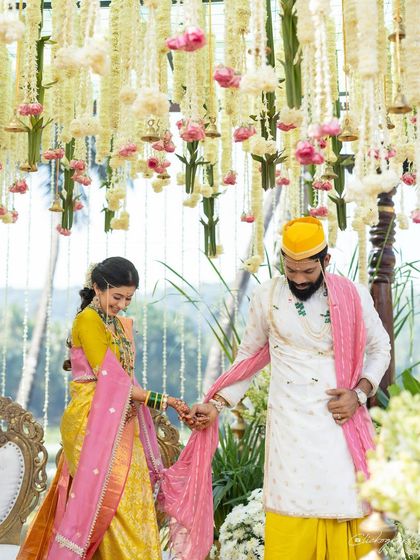 A beautiful ritual moment from a Konkan wedding. The bride's yellow saree with a pink border and shela creates a stunning visual against the lush green and floral decor.