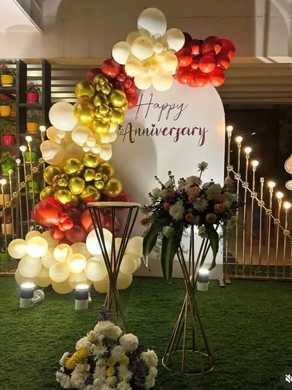 For this anniversary celebration, I used a custom white backdrop with 'Happy Anniversary' script. The decor is accented with a balloon garland in red, gold, and white, along with elegant floral stands.
