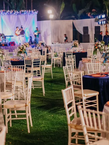 The outdoor reception area for ACE's communion. The lawn is set with round tables covered in silver and navy blue linens, with a live band performing on stage in the background.
