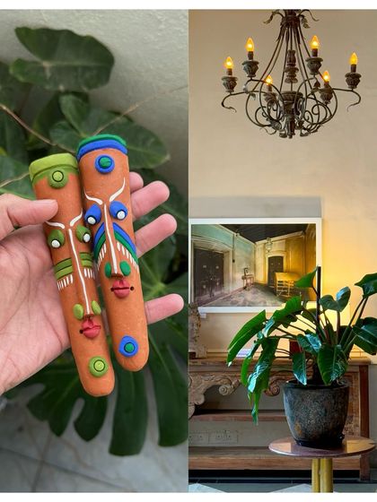 Handcrafted clay faces from a Pondicherry market, held against a backdrop of monstera leaves.