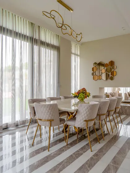 A wide shot of the elegant dining room, showcasing the striped marble floor, modern chandelier, and a view into the adjacent living area. The neutral color palette creates a calm and sophisticated atmosphere.