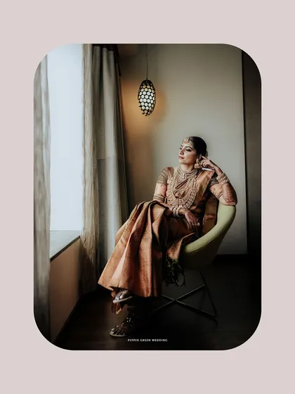 An elegant, pensive portrait of the bride seated by a window, her traditional attire looking stunning in the soft light.
