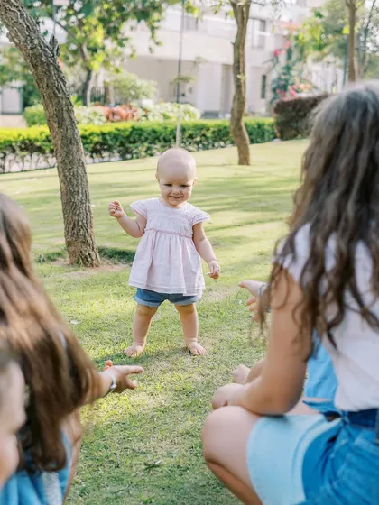 A baby girl taking her first steps towards her family. A huge milestone captured in a beautiful outdoor setting.