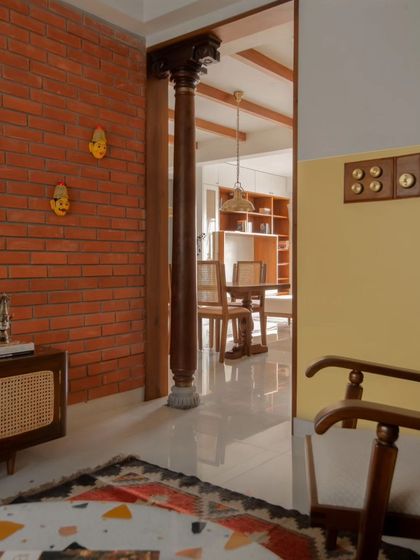A view from the foyer into the dining area, framed by an antique wooden column. This transition space uses color blocking and material changes, from brick to plaster, to define zones within the open layout.