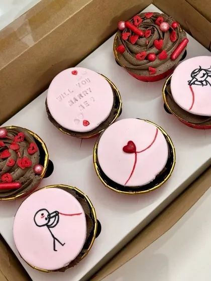 A box of Valentine's Day cupcakes, including a 'Will you marry me?' design and a cute red string of fate theme.