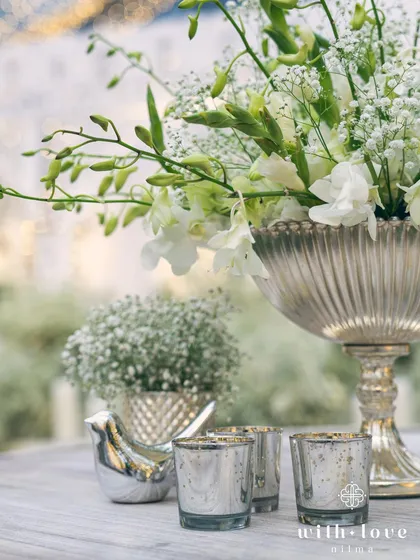 A table detail showing a silver bird ornament nestled among white flowers. These small, thoughtful touches add personality and charm to the event decor.