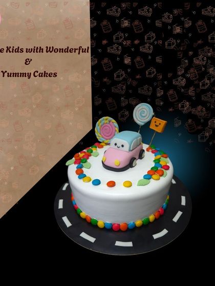 A cute and simple car-themed cake, showing a pink car on a road surrounded by colorful candies. A great choice for a toddler's birthday.