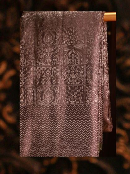 A close-up of the complex geometric and floral patterns woven in silver zari on the grey Kanjivaram.