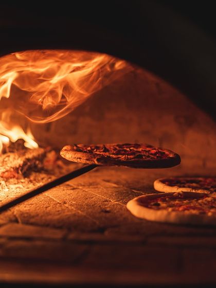A pizza bakes inside the intense heat of our wood-fired oven. You can see the flames licking the side of the oven, charring the crust perfectly.