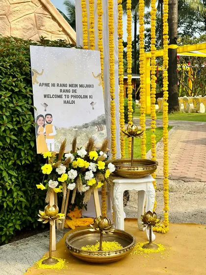 A personalized welcome corner for a 'Phoolon ki Haldi'. The setup includes a custom easel sign, brass urlis filled with flower petals, and elegant floral arrangements to greet guests.