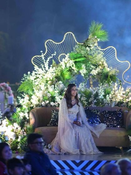 Grooving to the rhythm of love. A beautiful shot of the bride enjoying the Sangeet performances from a specially designed seating area, surrounded by lush floral decor.