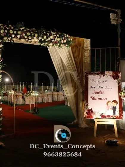 A beautiful night-time view of a wedding entrance. The floral arch, combined with a personalized welcome sign and warm lighting, creates a romantic and inviting entryway.