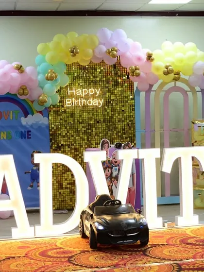 A pastel Cocomelon theme for Advit's first birthday, featuring a gold sequin wall, a rainbow on the backdrop, and a toy car for the birthday boy.
