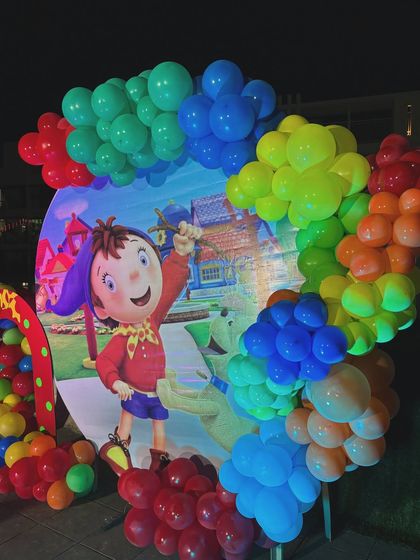 A nostalgic and colorful Noddy themed birthday party. The backdrop features the beloved character in Toyland, framed by a rainbow balloon arch.