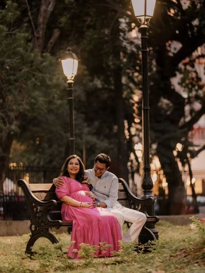 A quiet moment on a park bench at dusk. The warm glow of the lamps adds a romantic, storybook quality to this couple's maternity portrait, capturing the peaceful anticipation of waiting for their baby.
