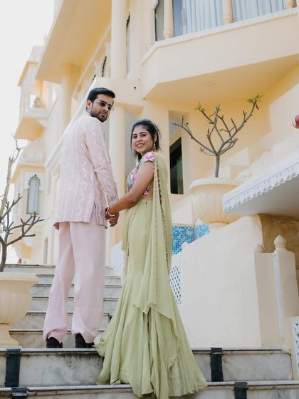 The couple looking back during their Welcome Lunch. This angle shows the beautiful flow of her ruffled saree and the elegant embroidery on the back of his pastel pink jacket.