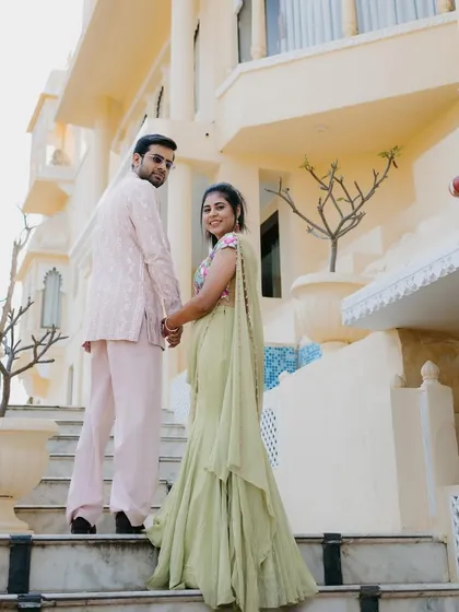 The couple looking back during their Welcome Lunch. This angle shows the beautiful flow of her ruffled saree and the elegant embroidery on the back of his pastel pink jacket.