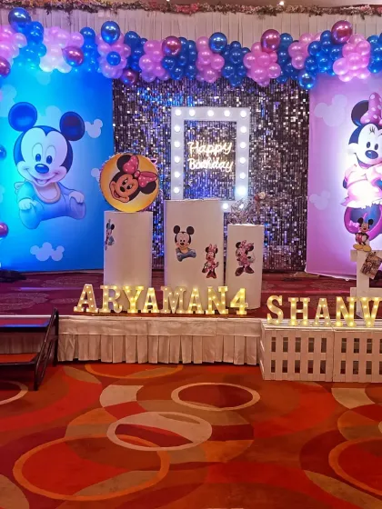This is a complete stage setup for a Mickey and Minnie Mouse themed birthday party. We included character backdrops, a central sequin panel with a "Happy Birthday" light box, and personalized light-up names for the birthday kids, Aryaman and Shanvi.