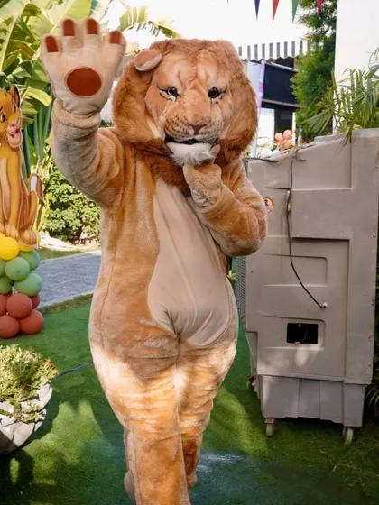 A life-sized Simba mascot from The Lion King waves to guests at a jungle-themed party.