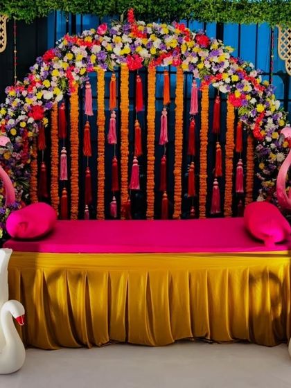 A fun and quirky Mehandi seating arrangement with swan and flamingo props. The backdrop is a mix of a floral arch and colorful tassels, creating a playful and vibrant setting.