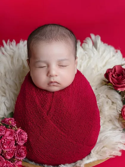A bold and beautiful setup with a newborn wrapped in red, surrounded by matching roses.