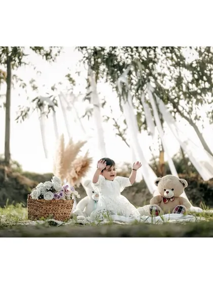 Waving with excitement during her forest picnic. The flowing white ribbons in the trees add a touch of whimsy to this joyful outdoor shoot.