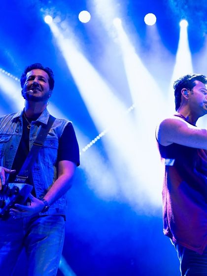 The composer-singer duo Salim and Sulaiman Merchant performing together under dramatic blue lighting. We are experts in managing shows with multiple lead artists.