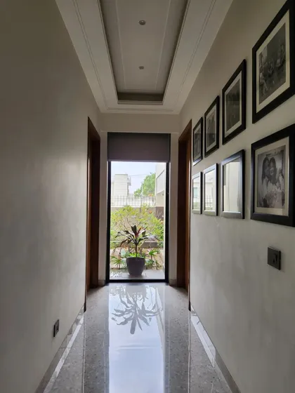 In this hallway, we created a direct axis to the outdoors. The passage terminates with a full-length glass door, drawing the eye towards the greenery and flooding the corridor with natural light, making the space feel open and connected.