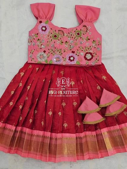 A lovely red and pink combination for a toddler. The blouse features colorful floral embroidery, and the skirt has a simple gold border.