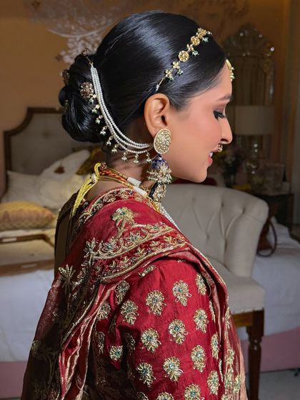 A side view of a classic bridal bun, accessorized with a pearl and gold hair chain (matha patti) and small floral clips for a traditional look.