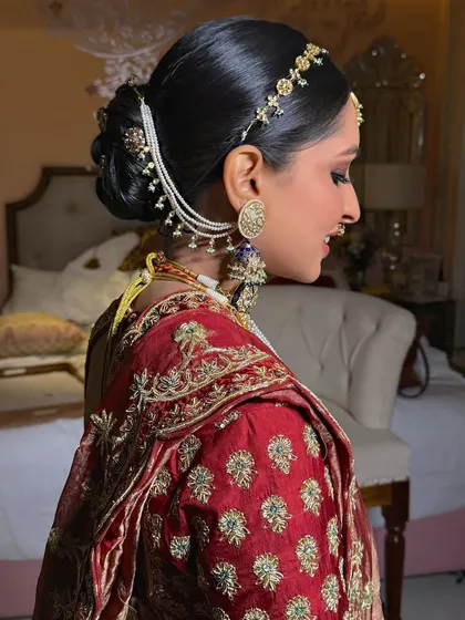 A side view of a classic bridal bun, accessorized with a pearl and gold hair chain (matha patti) and small floral clips for a traditional look.