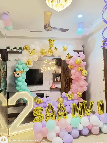 A beautiful pastel-themed 2nd birthday for "SAANVI". This living room setup includes a balloon arch in mint, pink, and lavender, gold foil name balloons, and a large light-up number '2'.