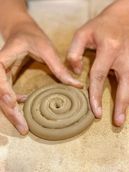 A student carefully forms a coil of clay, getting it ready to be added to their growing hand-built piece.