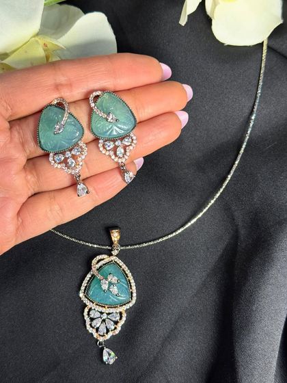 This pendant set features a unique triangular design with a carved sea-green stone. The dangling teardrop stone adds a touch of movement and sophistication, making it a modern and stylish choice.