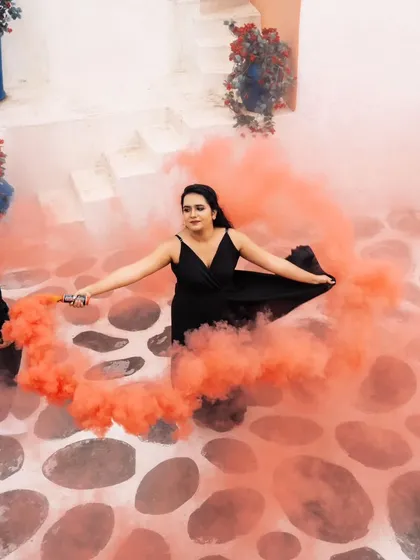 A dramatic overhead shot of a woman in a black dress creating a swirl of orange smoke around her. This creative use of a smoke bomb and a unique angle results in a stunning, artistic photo.