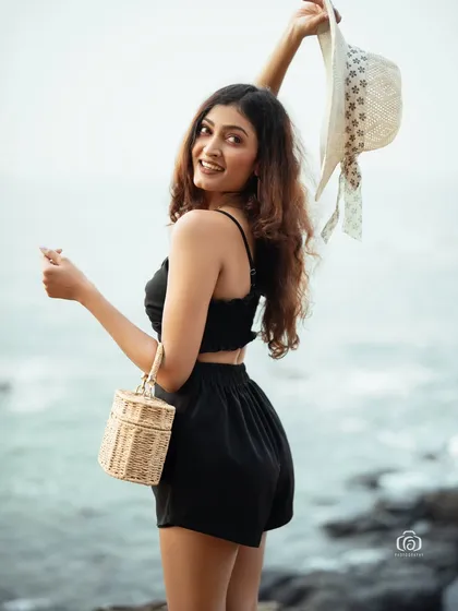 A playful and happy moment captured on the beach. The model is holding up her sun hat, creating a fun and energetic image that feels spontaneous and natural.