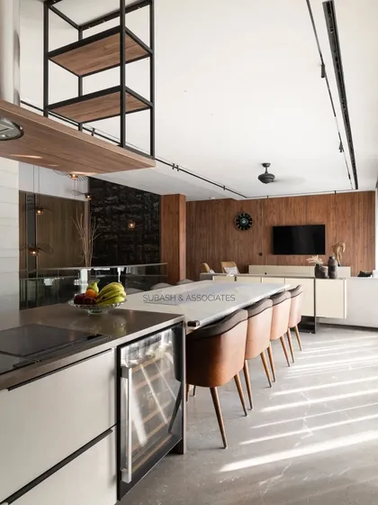 The open kitchen features a large island with seating, seamlessly connecting to the lounge area. Ample daylight highlights the natural textures of the materials.