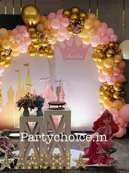 A beautiful princess castle theme in pink and gold. This elegant setup includes a large balloon arch, a backdrop featuring a castle silhouette, and a cutout of Princess Ariel.