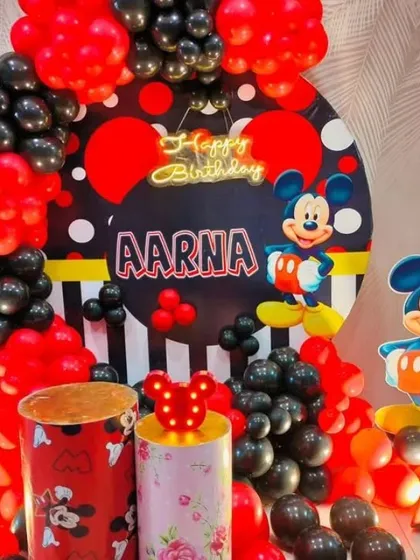 A Mickey Mouse themed birthday party with a red and black balloon arch. The setup includes a custom backdrop and Mickey-themed pedestals.