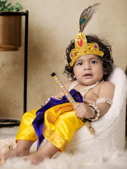 A classic seated portrait of a toddler dressed as Krishna, holding his flute. The professional studio-like setup was created entirely within the client's home.