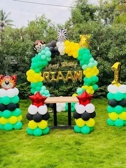 An outdoor jungle-themed first birthday with balloon columns topped with animal faces and a central balloon arch.