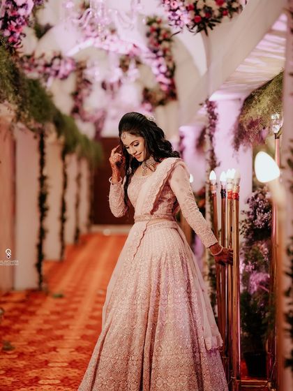 A full-length shot of a bride in a pink lehenga, captured in a beautifully decorated hallway.