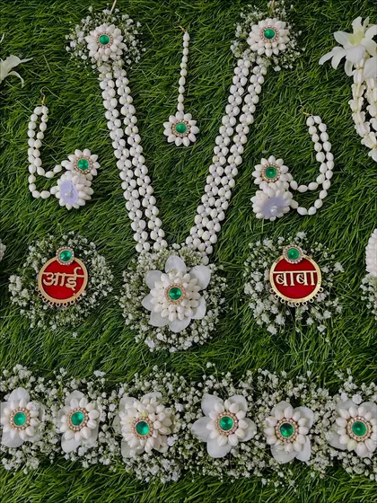 A close-up of a custom Dohale Jevan set with green stone accents. The set includes personalized 'Aai' and 'Baba' brooches, a kamarband, necklace, and earrings.