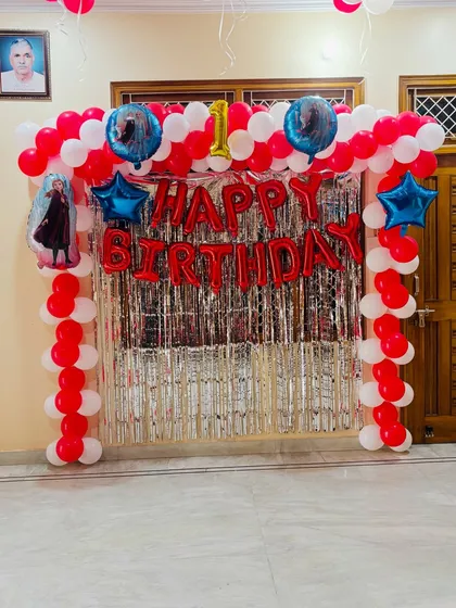 A Frozen-themed first birthday party decoration. This setup has a red and white balloon arch with characters from the movie and a silver shimmer curtain.