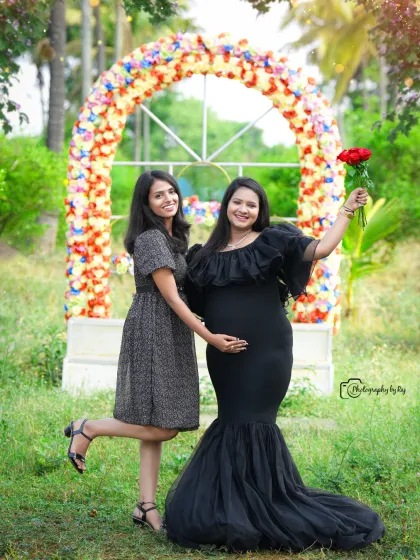 A fun and joyful outdoor portrait with a friend. The mother-to-be is wearing a black mermaid-style gown and holding a single red rose.