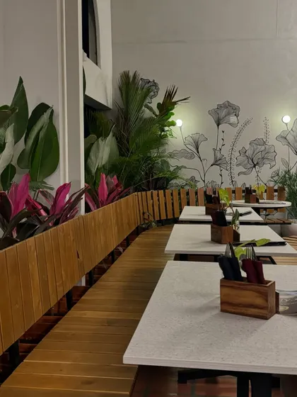 The combination of wooden planters, vibrant pink Aglaonema, and a floral wall mural creates a unique and artistic ambiance in this cafe. My designs often integrate with other decor elements.