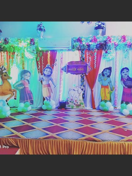 A Krishna-themed naming ceremony stage with character cutouts against a backdrop of curtains and lights, creating a simple yet beautiful setup.